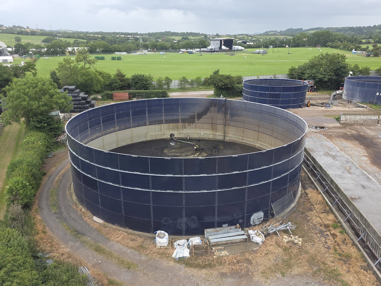 About Aerial photo showcasing large industrial water tanks amidst lush countryside landscape under cloudy sky.
